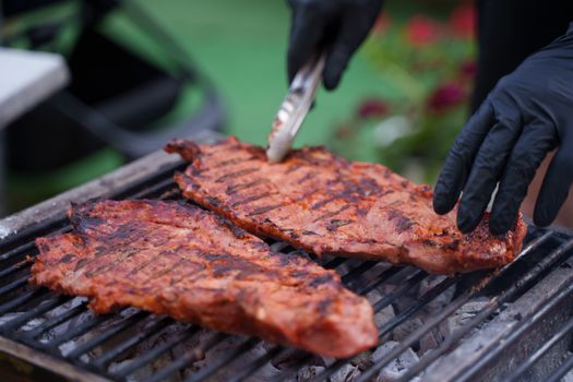 Close-up of juicy steaks grilling on an outdoor barbecue with gloved hands flipping meat.