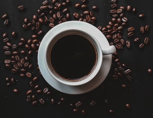 Top View of a Cup of Black Coffee with Scattered Coffee Beans on the Table 