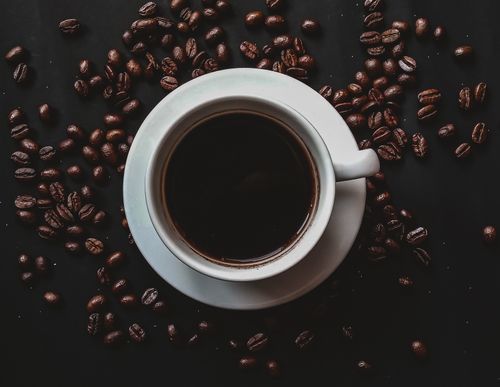 Free Aesthetic top view of black coffee in a white cup surrounded by coffee beans. Stock Photo