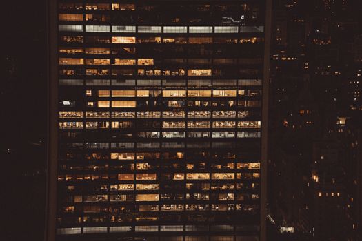 Aerial view of a lit skyscraper in New York City at night, showcasing urban office life.