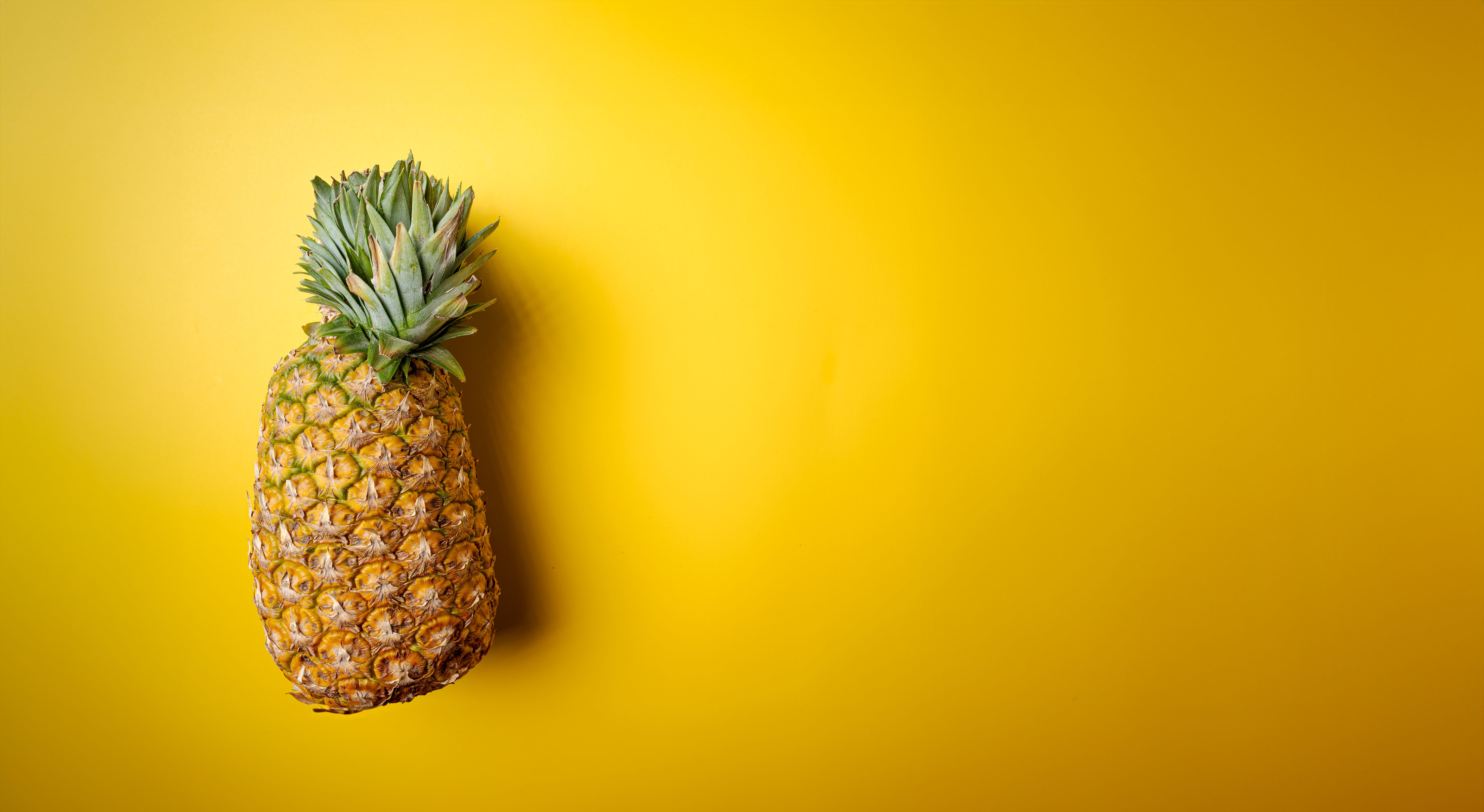 A fresh tropical pineapple placed against a vibrant yellow background, offering copy space.