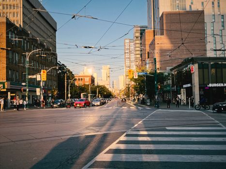 Bustling city street intersection with overhead lines and traffic at sunset.