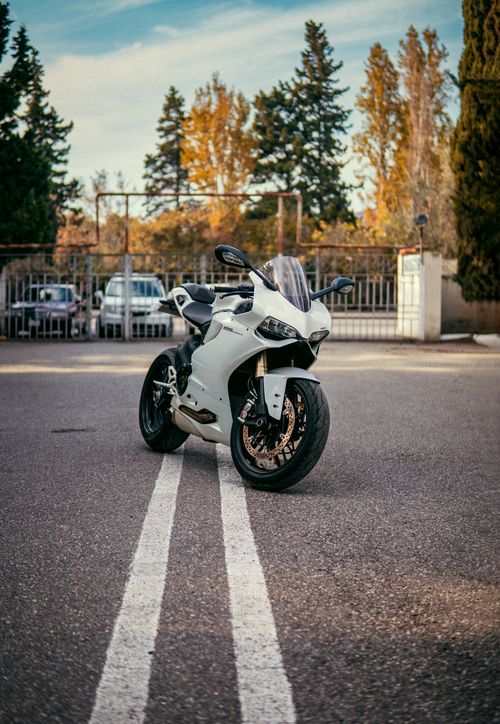Free A sleek white sport bike parked on city streets with autumn foliage in the background. Stock Photo