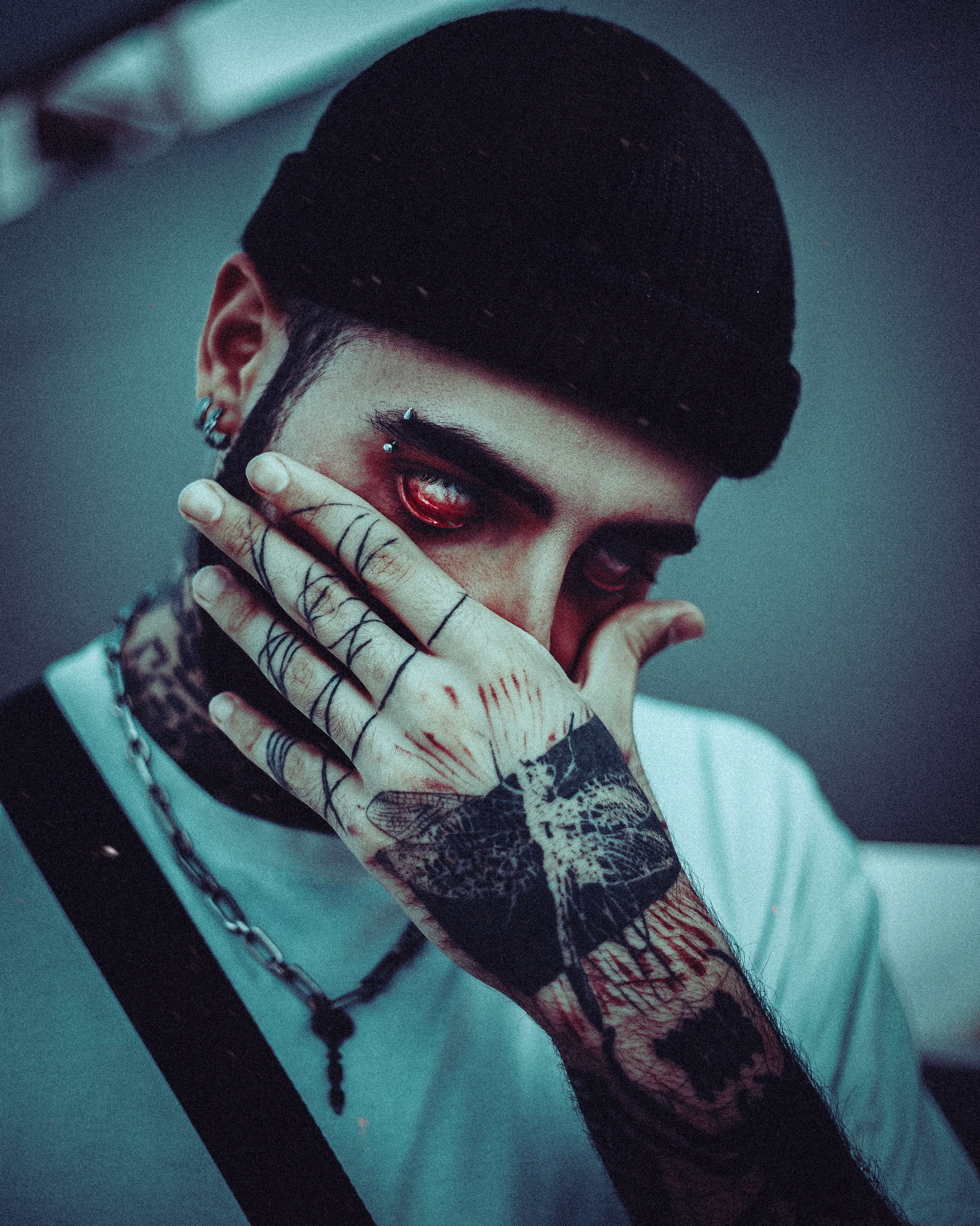 Close-up portrait of a tattooed man wearing a beanie and piercings, hand covering face.