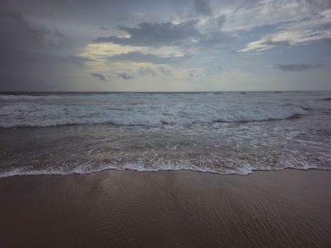 Peaceful ocean waves gently crashing on a quiet beach at dawn under a dramatic sky.