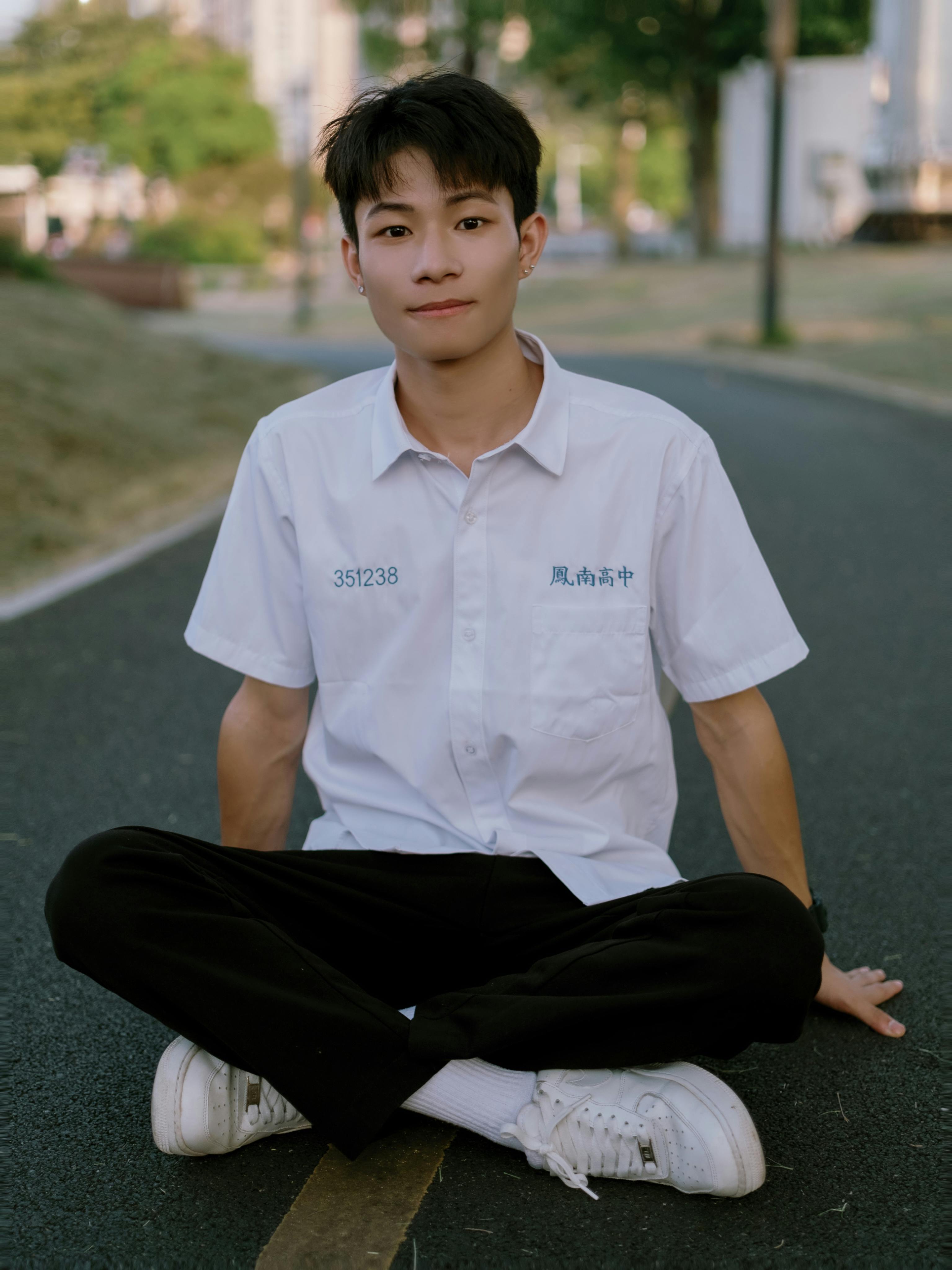 A young man in a casual pose on a city street in daylight, wearing a school uniform.