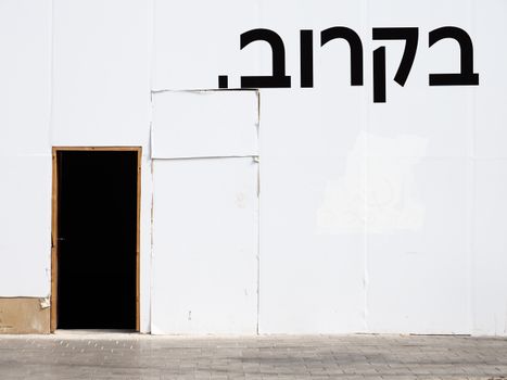 Simple white wall with a black door and Hebrew text, offering urban minimalism.