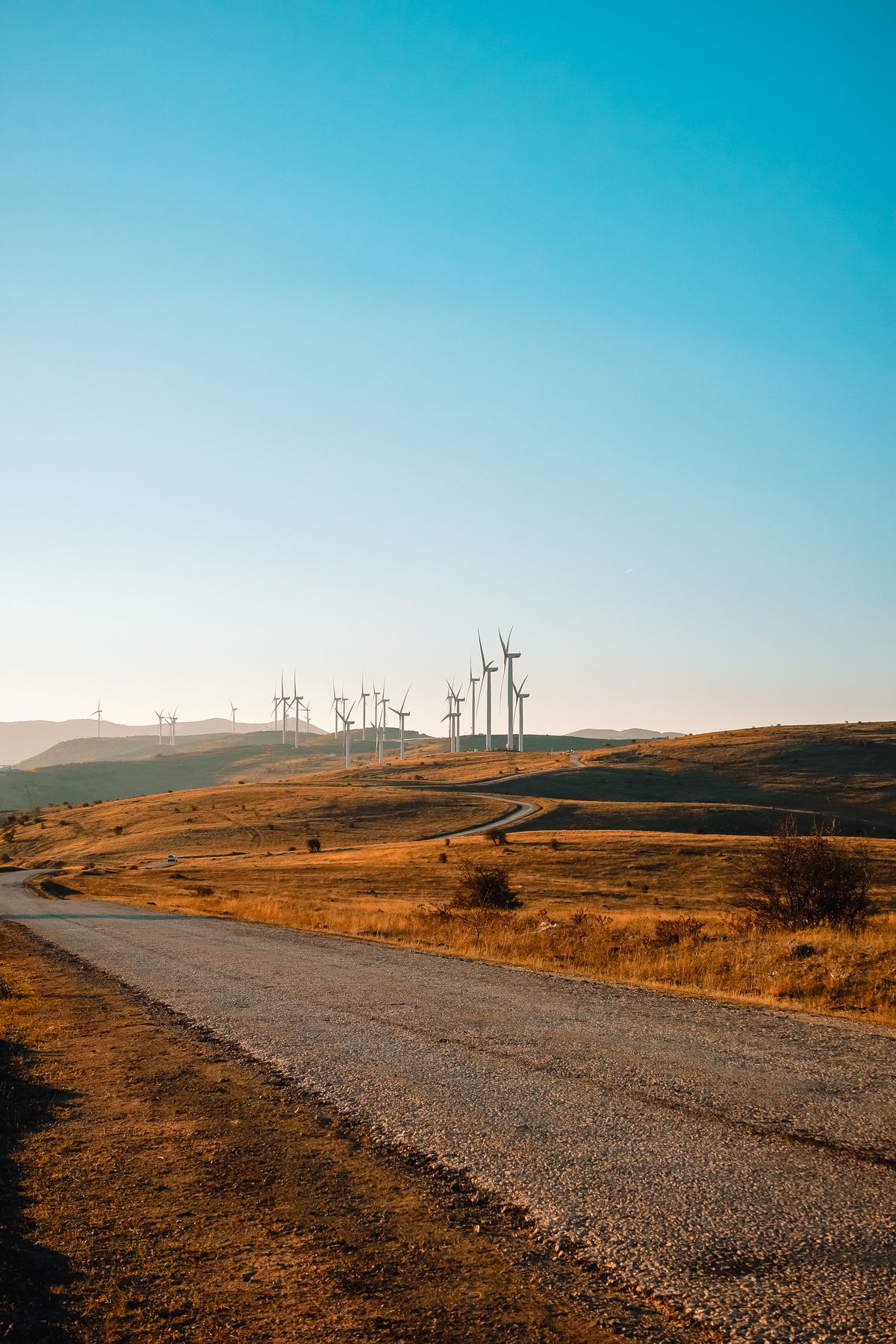 Wind turbines on hills beside a winding road, a generating facility tracked through mitigation milestones to completion