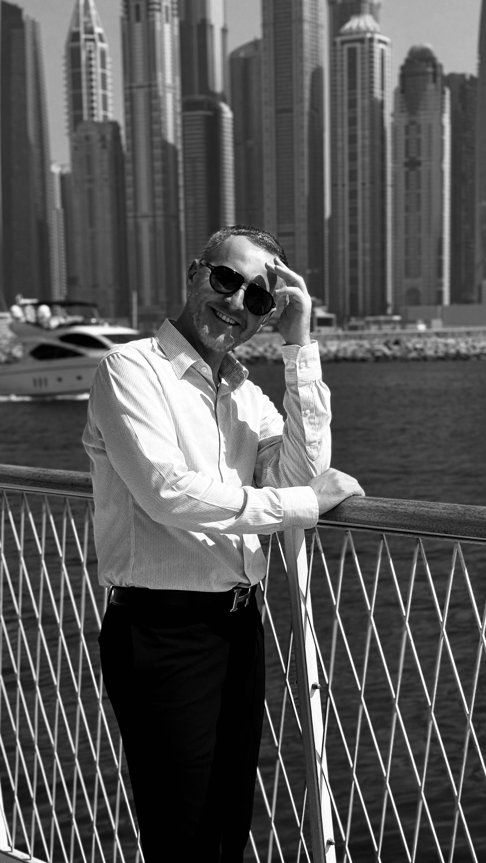 Fashionable man posing in urban setting with a modern city skyline in the background.
