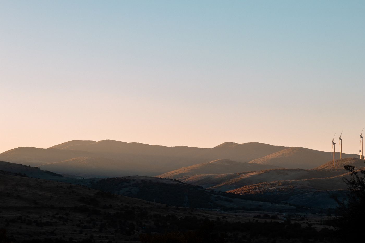 Beautiful landscape at sunset with wind turbines silhouetted against rolling hills, showcasing renewable energy in nature.