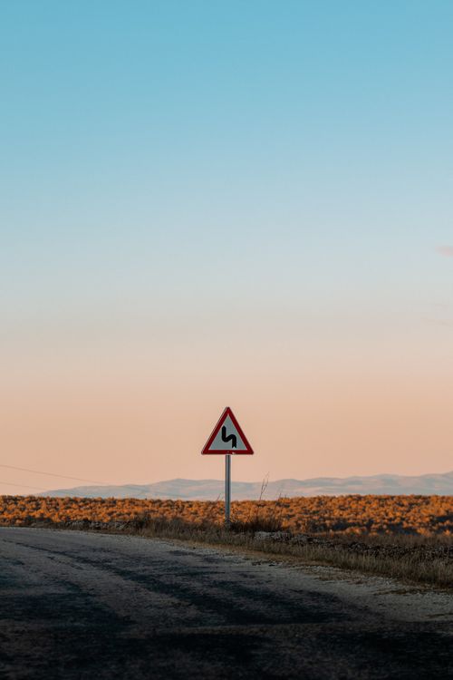 Free Scenic view of a road sign indicating curves ahead, under a stunning sunset sky. Stock Photo