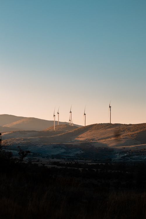 Free A serene landscape with wind turbines on rolling hills at sunset, showcasing renewable energy. Stock Photo