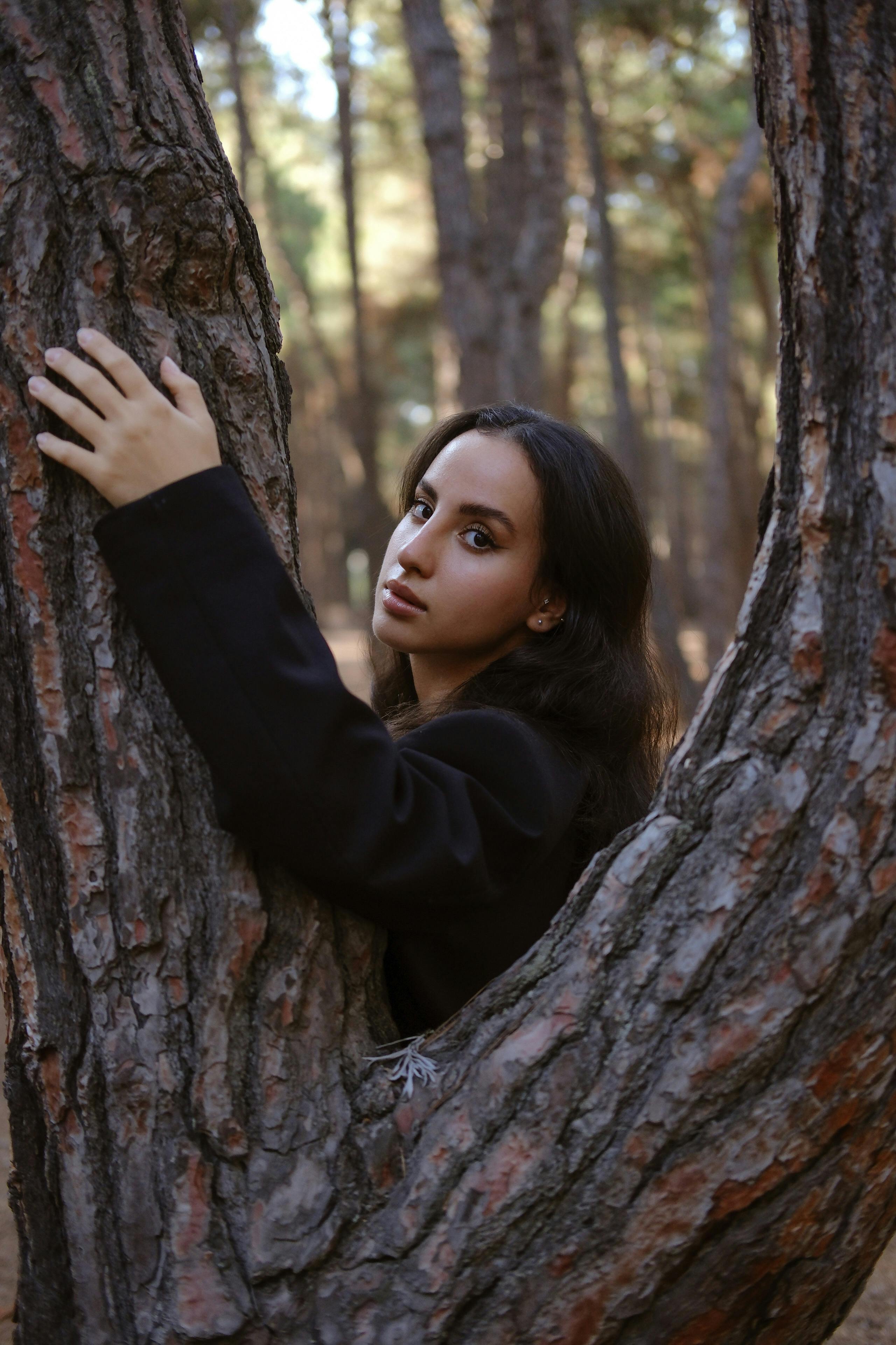 a woman is leaning against a tree in the woods