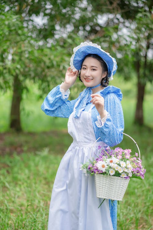 Smiling Woman in Blue Dress, Hat and with Basket of Flowers