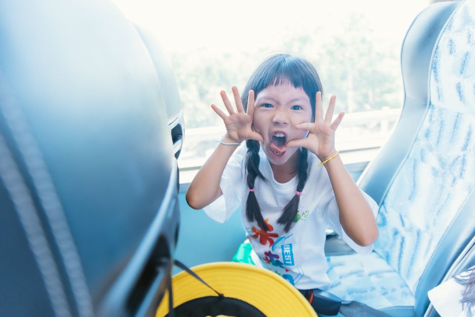 A playful young girl making faces while traveling on a bus, capturing the essence of childhood fun.