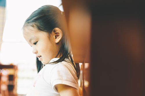 Free A serene portrait of a young girl in profile, thoughtfully looking down in a warmly lit indoor setting. Stock Photo