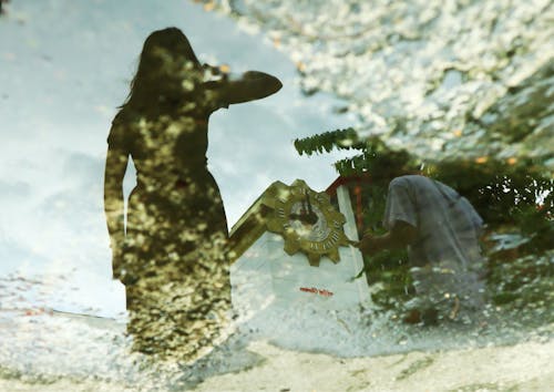 Reflection of Woman, Man and Building in Puddle