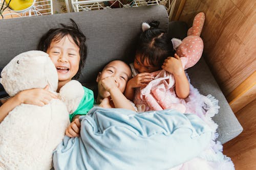 Children Lying on a Sofa with Teddy Bears and Smiling 