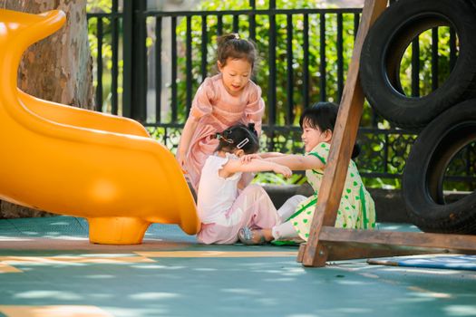 Three children playing joyfully near a vibrant yellow slide on a sunny day at the outdoor playground.