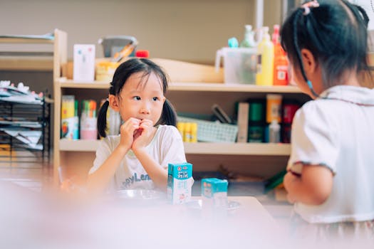 Two young Asian girls in a classroom setting enjoying milk cartons, showcasing school innocence.