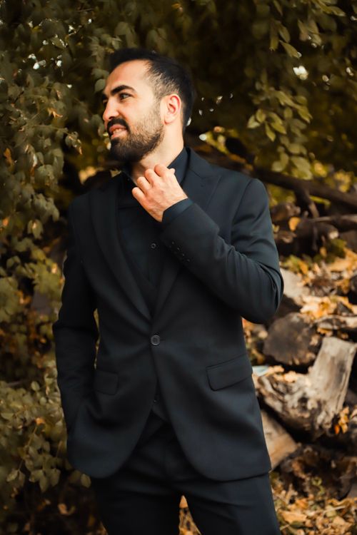 Free Stylish man in a black suit posing confidently in a natural forest environment. Fashion portrait. Stock Photo