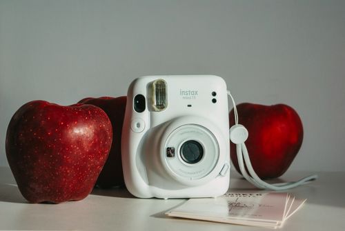 Free A still life composition featuring an Instax camera surrounded by red apples, conveying a blend of technology and nature. Stock Photo