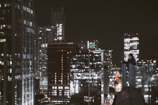 夜晚，一个人站在屋顶，俯瞰着周围灯火通明的摩天大楼和繁华的城市景观