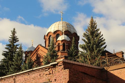 Free A striking Orthodox church dome amidst trees and brick wall under a vibrant blue sky. Stock Photo