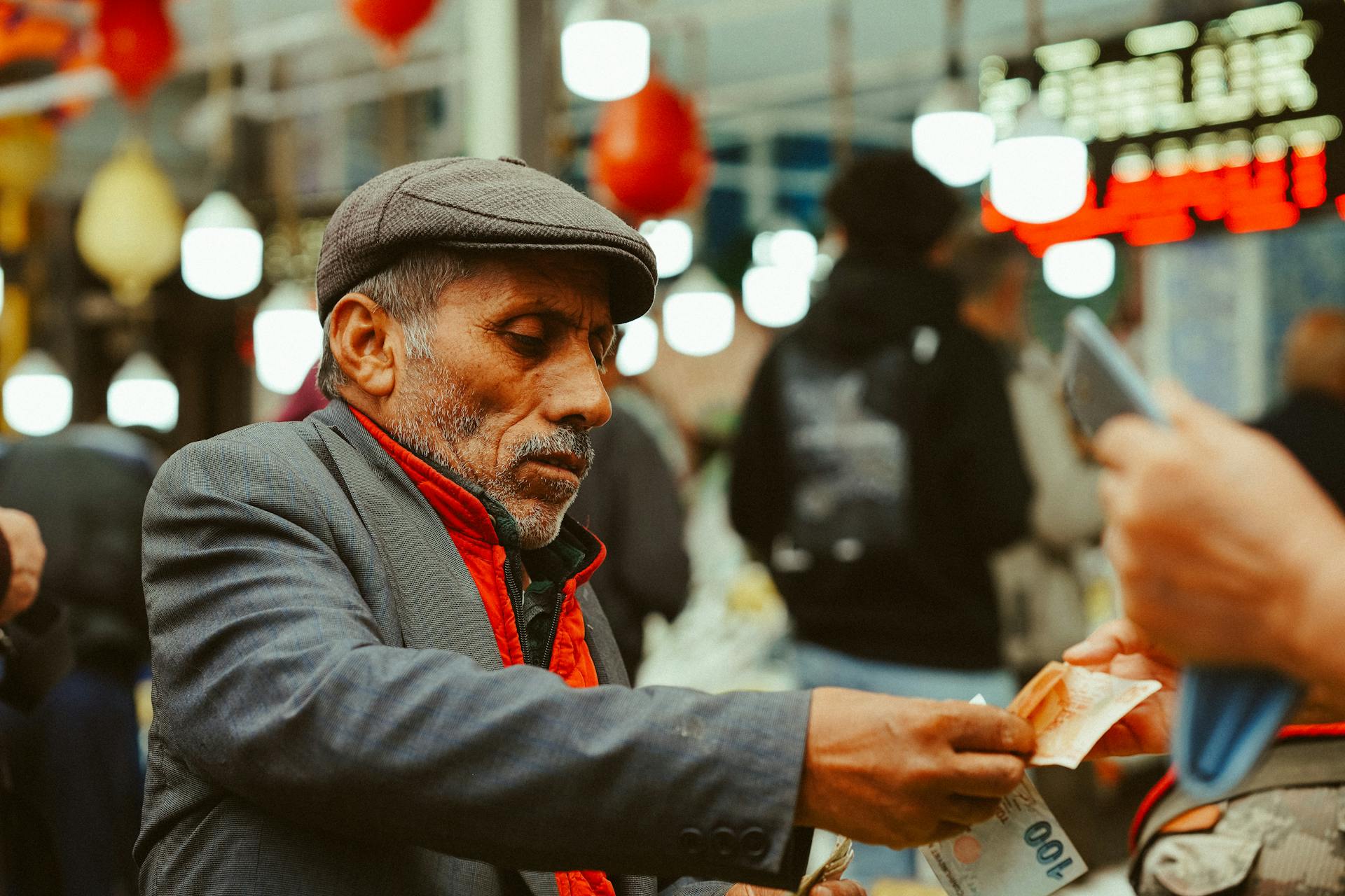 An elderly man with a flat cap exchanging money at Ankara's bustling market.