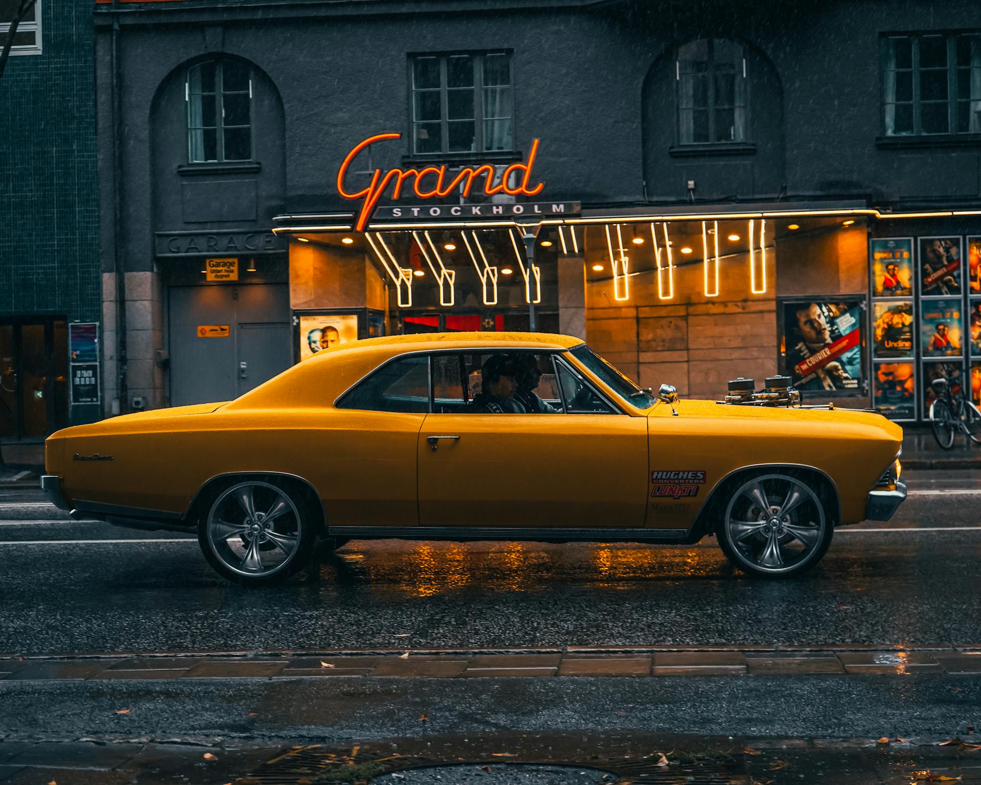 A classic yellow car parked on a rainy street in Stockholm, Sweden, outside the Grand Stockholm theater.