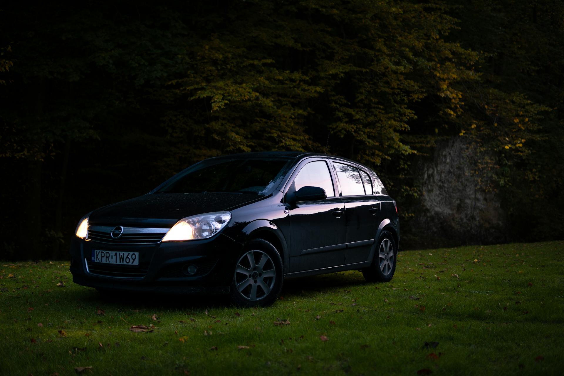 Black Opel Astra parked on grassy field in Skała, Poland during twilight.