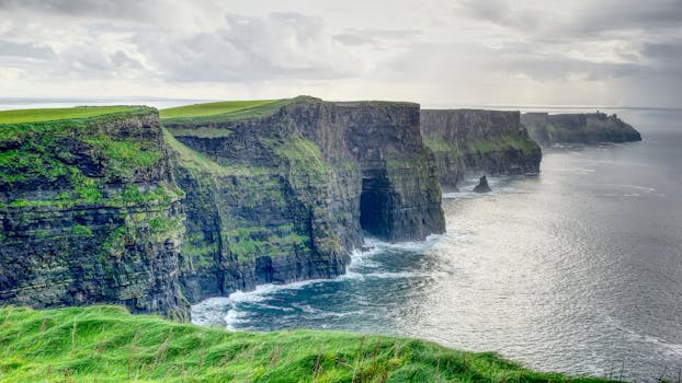 Breathtaking view of the Cliffs of Moher with lush green cliffs and waves crashing below.