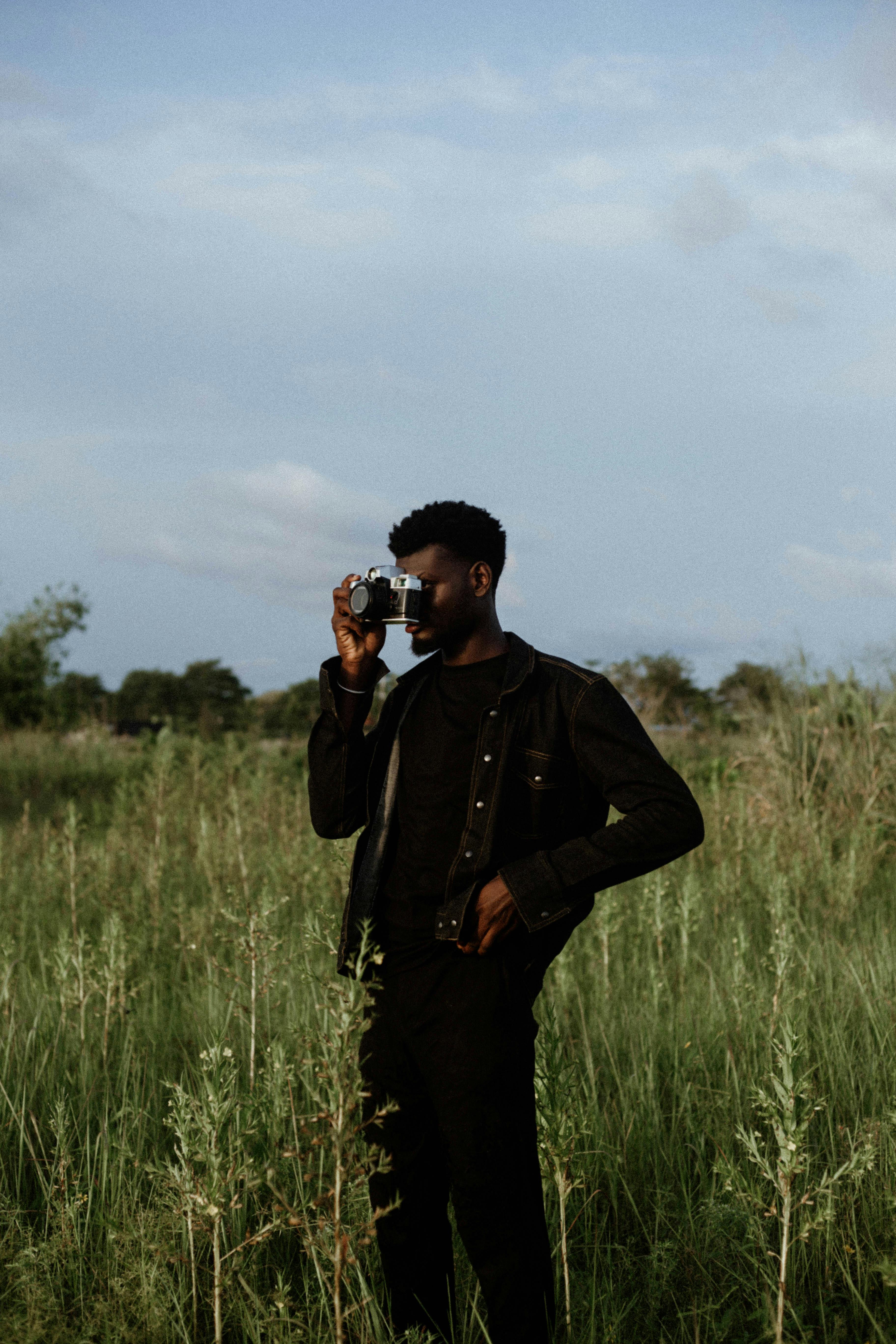 A man with a camera captures nature in a grassy rural field at dusk, creating a tranquil scene.