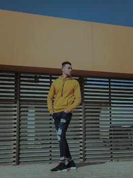 一名穿着时尚黄色毛衣的男子在现代户外背景下摆姿势