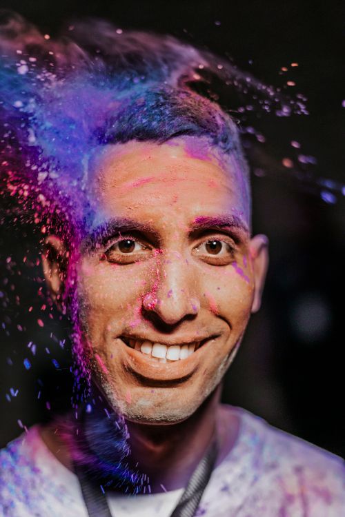 Free A man joyfully embraces vibrant colors during a festive celebration, enveloped in vivid powder. Stock Photo