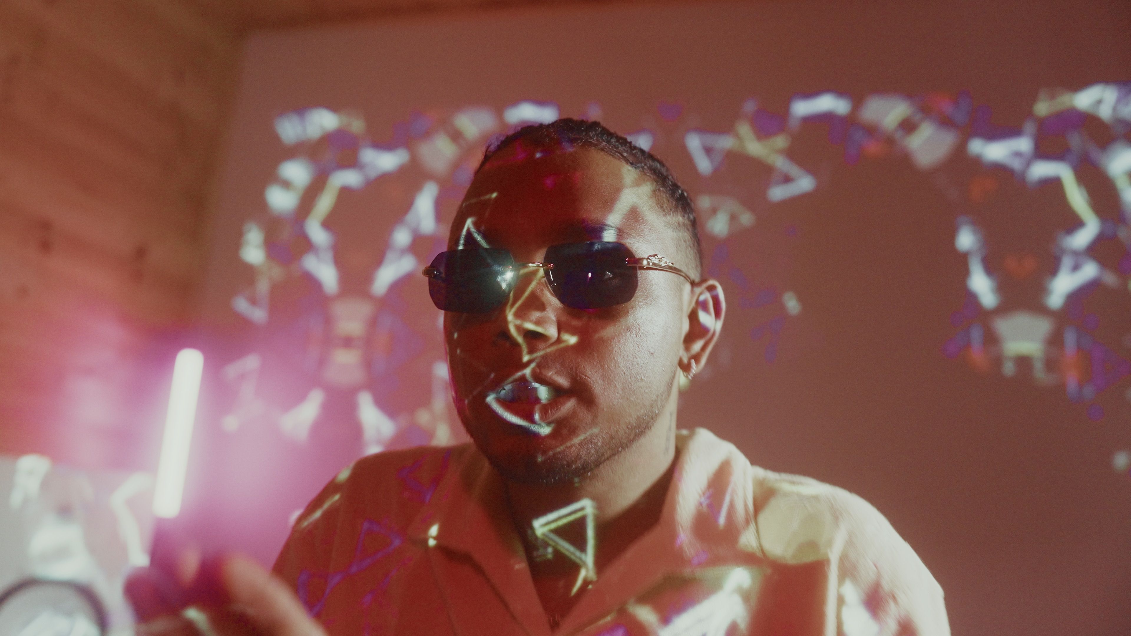 Man wearing sunglasses with vibrant geometric patterns projected on him, indoors.