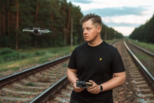Man piloting a drone with controller on railway tracks in a forested area.
