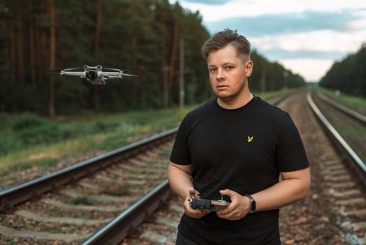Man controls drone on railway tracks in a rural forest setting. Technology meets nature.