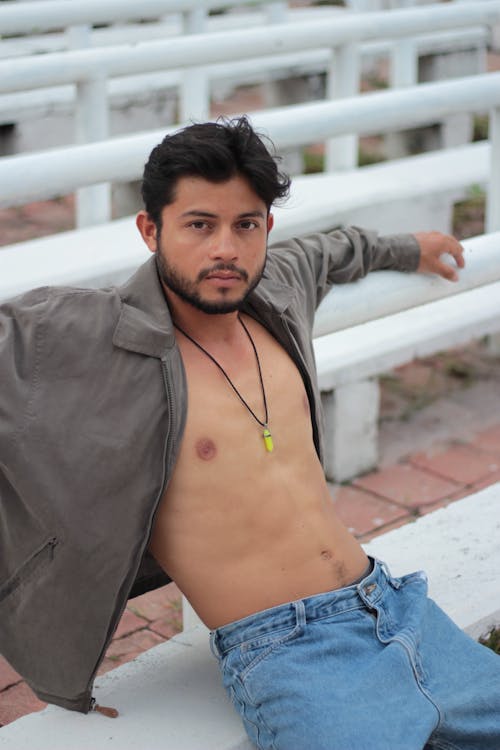Shirtless Model in an Gray Jacket and Jeans Sitting on a Bench