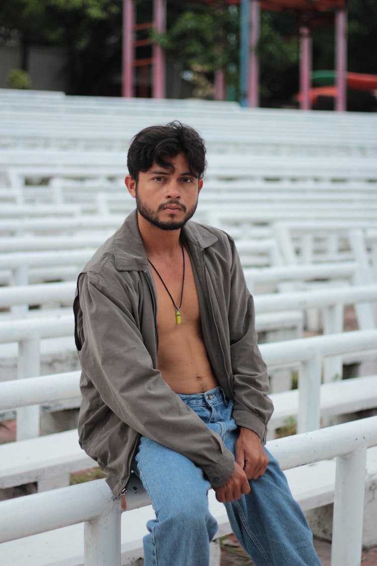 Shirtless Man Sitting On White Bleachers In Park