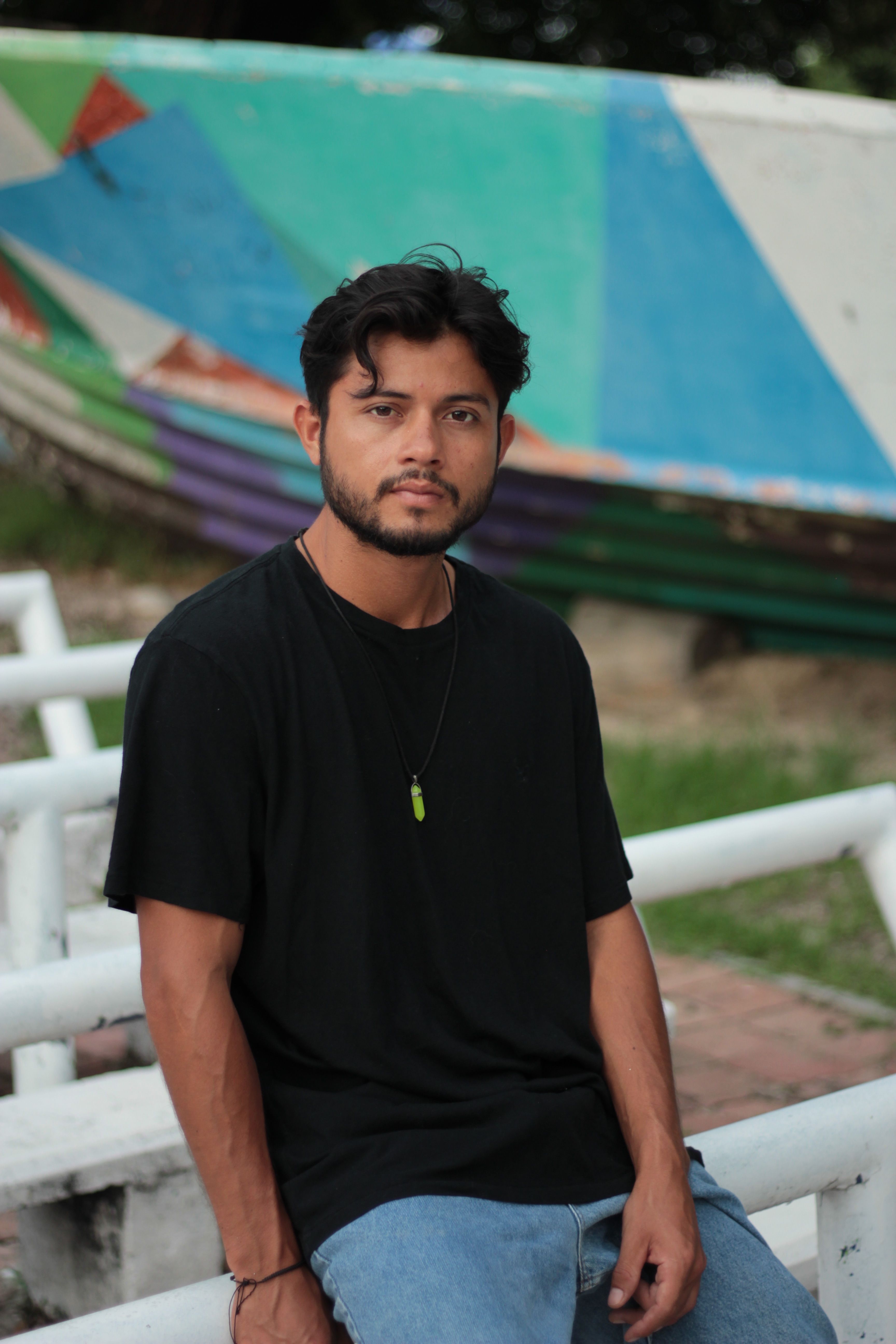 Young man in a black shirt sitting outdoors with colorful background.