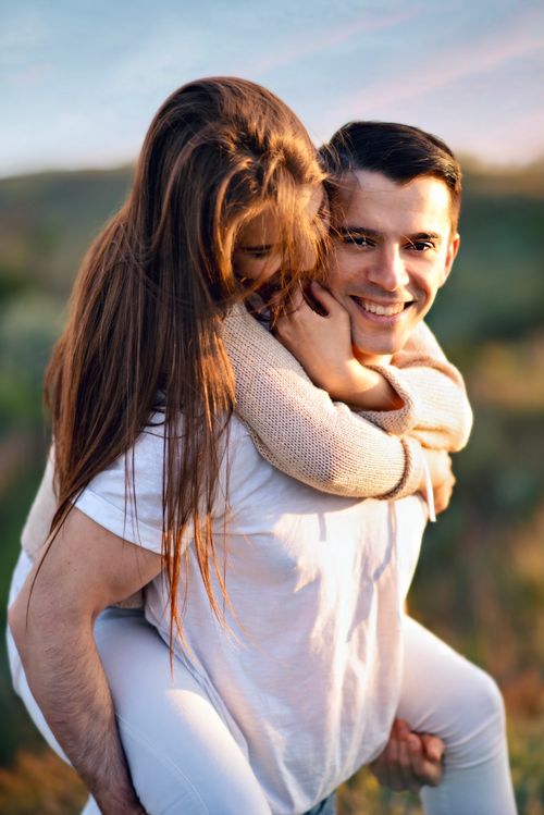 Free Happy couple enjoying a playful piggyback ride outdoors at sunset. Stock Photo