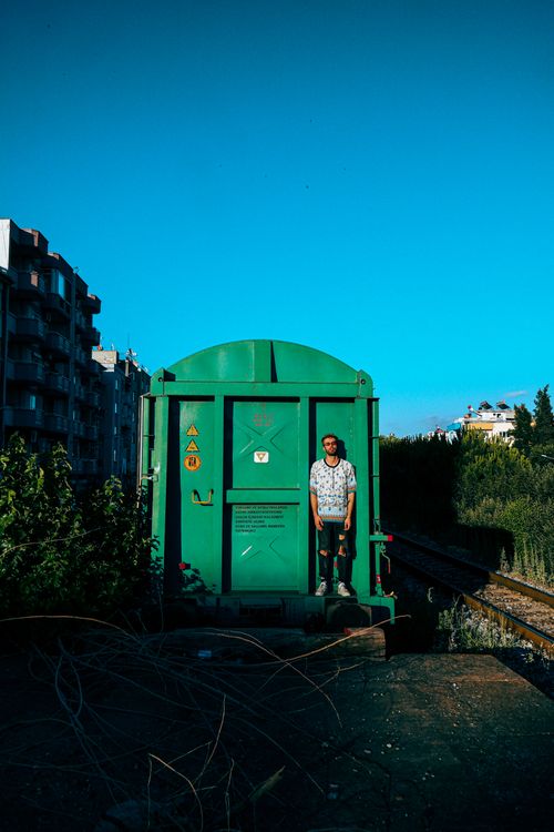 Free A man standing by a green cargo train car on a sunny day in the city. Stock Photo