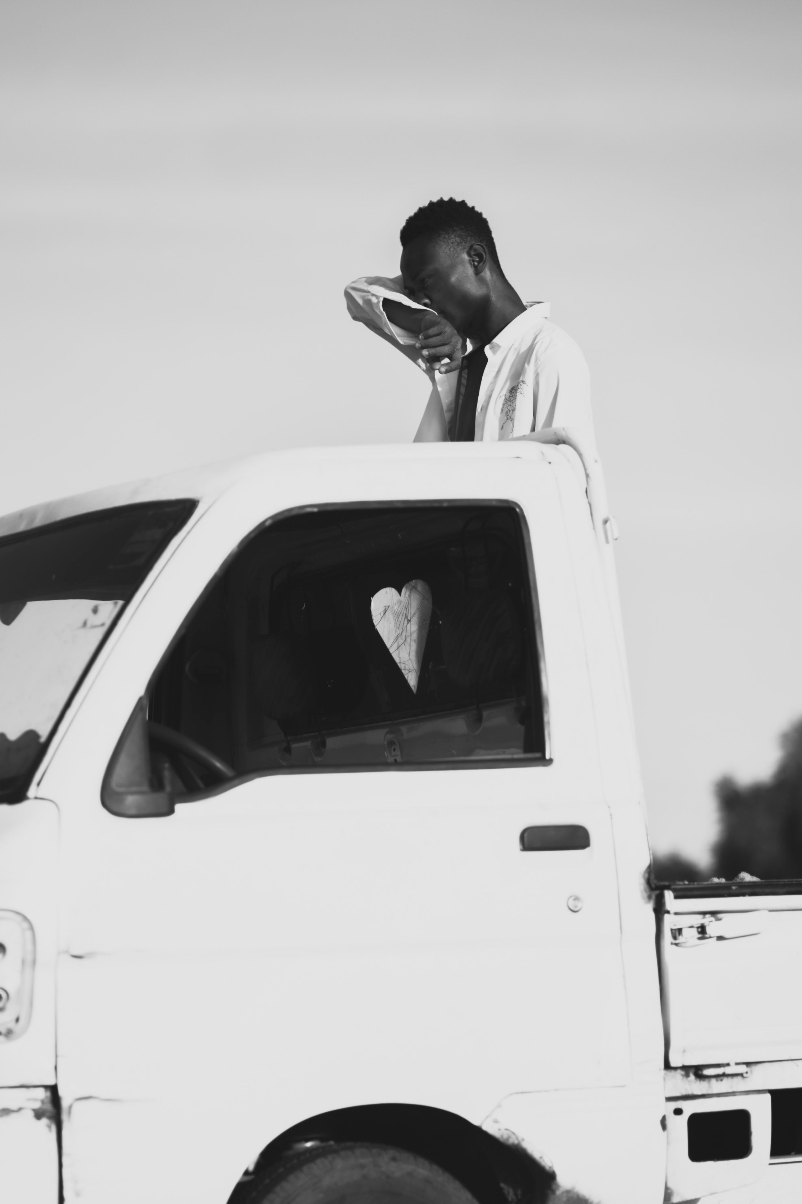 A black and white image of a man leaning on a truck, capturing a thoughtful mood.