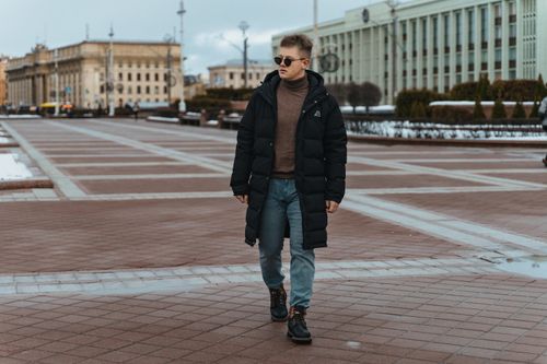 Free A man in a black coat walks confidently through a city square. Stock Photo