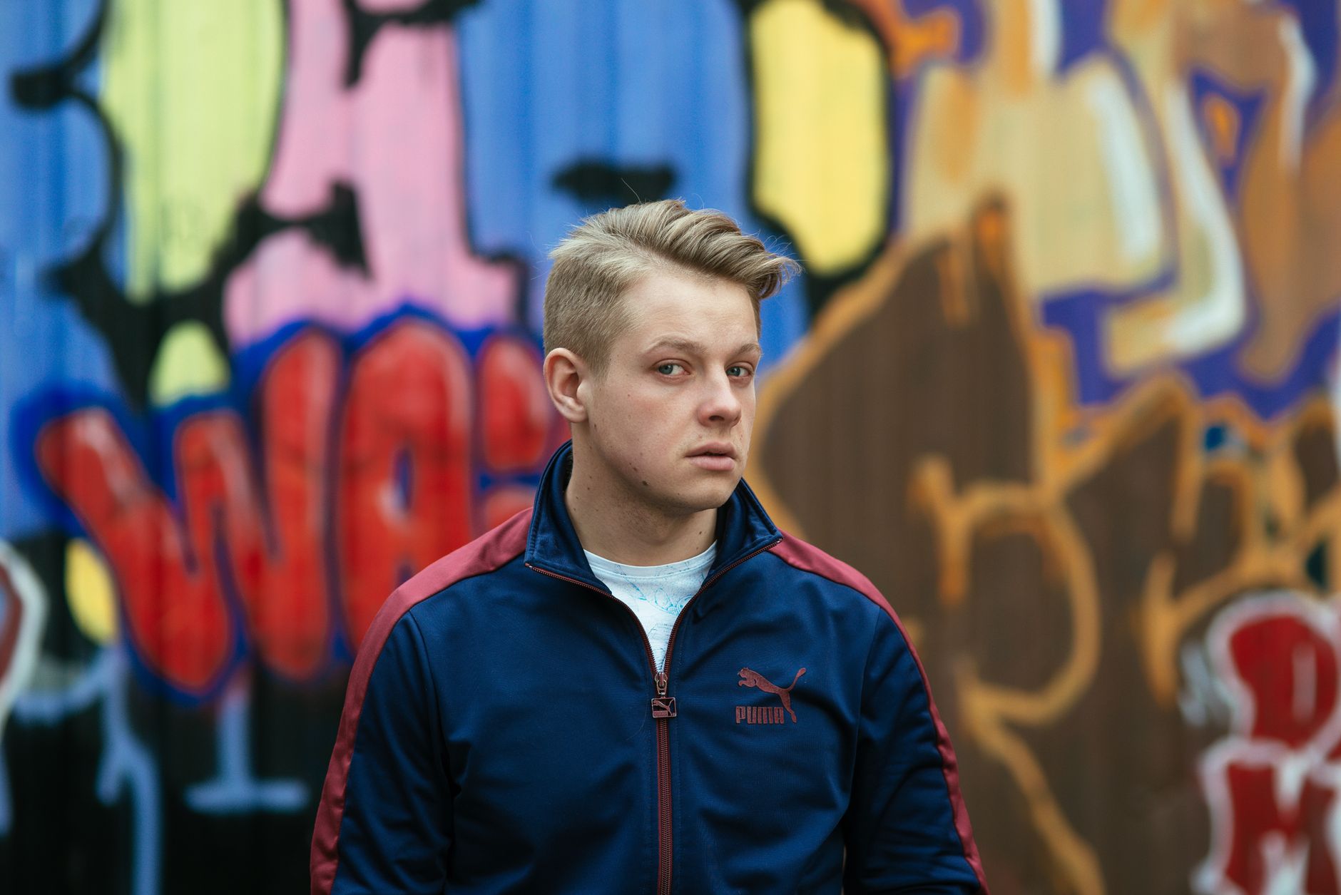 A young man in front of vibrant graffiti, embodying urban street style.