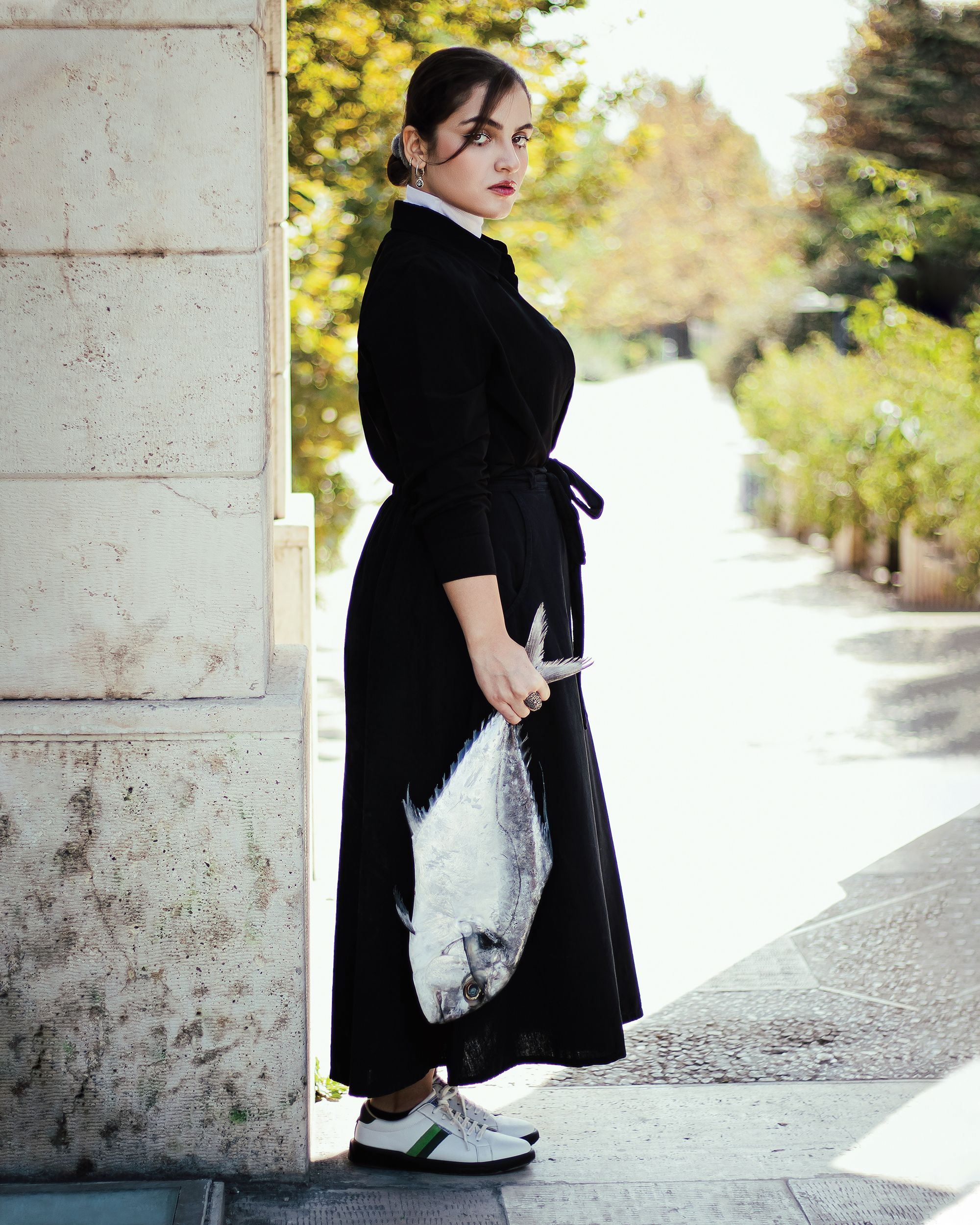 Elegant woman in a long black dress holding a fish, posing outdoors in Tehran.