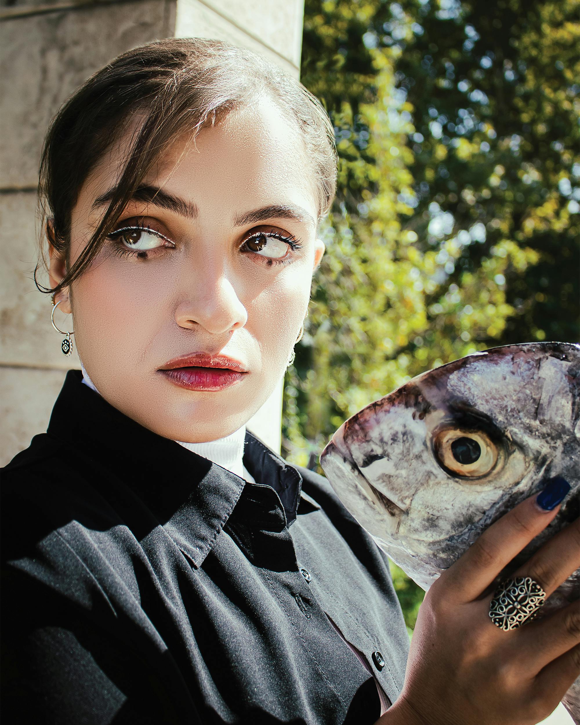 A young woman holding a fish while posing outdoors in Tehran, Iran.