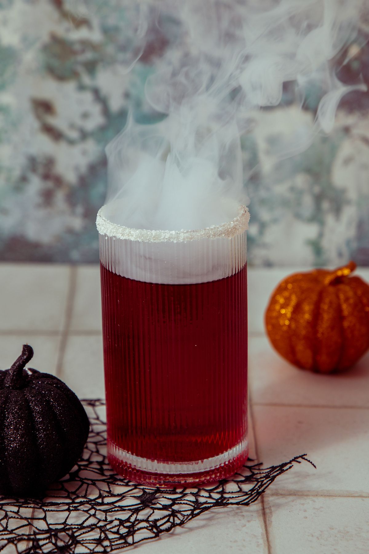 Steaming red cocktail glass surrounded by Halloween pumpkin decorations