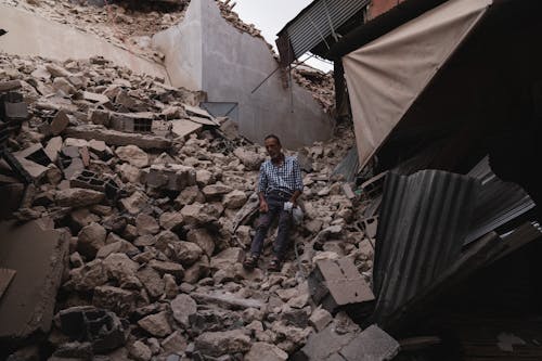 Man Sitting amid Rubble of a Destroyed House